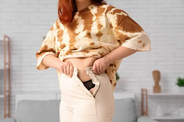 Image of woman trying to do her trousers up after pregnancy weight gain Alcester