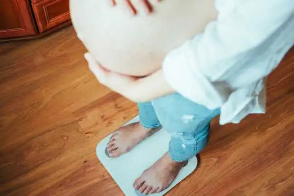 Image of woman weighing herself and experiencing weight gain through pregnancy Alcester